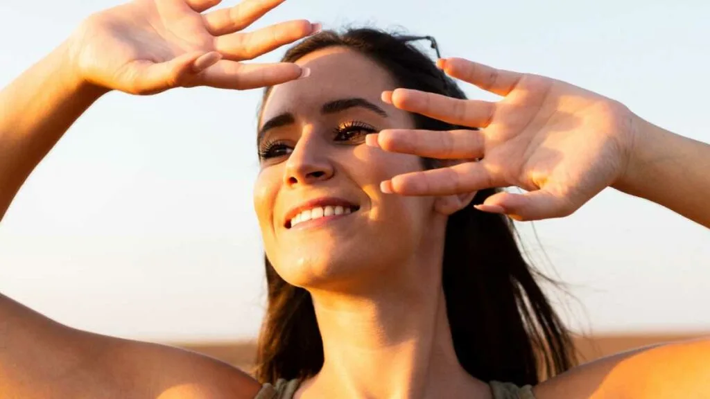 Mulher sorrindo protegendo o rosto do sol com as mãos