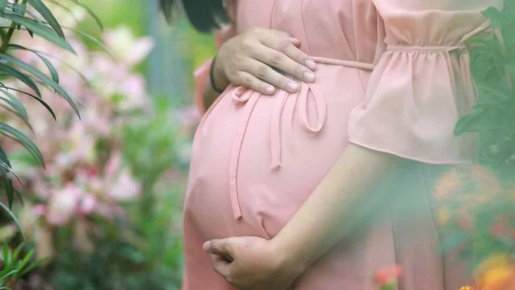 Mulher grávida com as mãos sobre a barriga, em vestido rosa